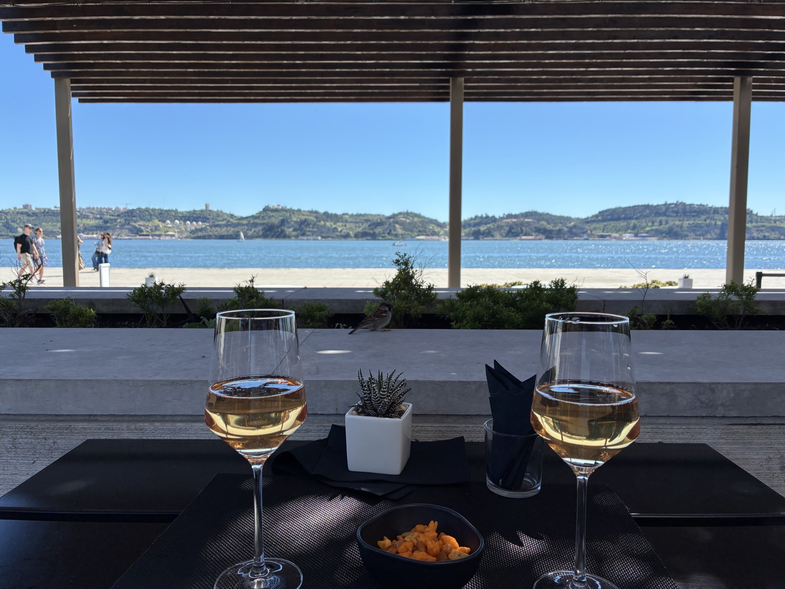 Two glasses of rosé on a table at a riverside café in Belém, Lisbon, with the Tagus beyond.